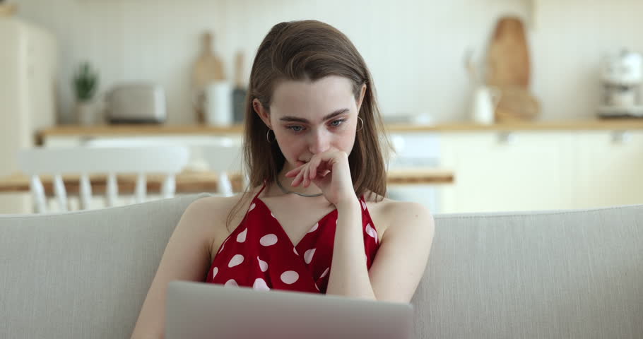 Pensive young pretty woman sits on sofa staring at laptop screen search solution, considers, thinks over difficult task while make assignment or working at home using internet and wireless computer Royalty-Free Stock Footage #1100087681
