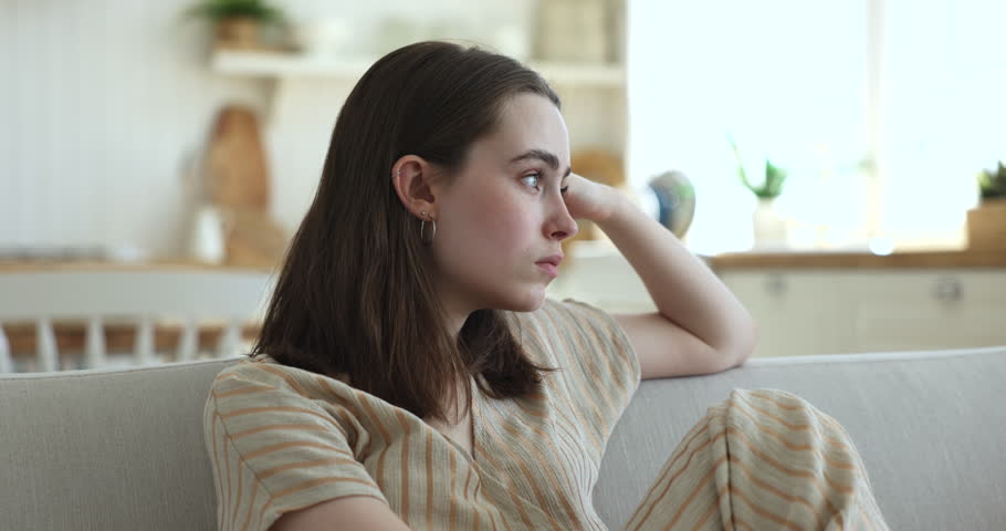 Lost in sad thoughts girl sit on couch, thinks, staring into distance feels emptiness by personal concerns, looks lonely and frustrated, having bored weekend alone at home. Low self-esteem, problems Royalty-Free Stock Footage #1100087729