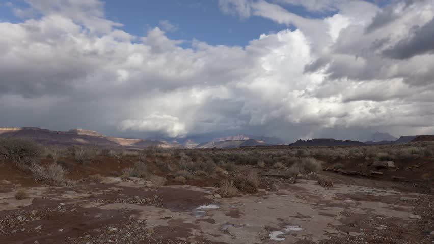 Time lapse video with small puddles scattered along the bottom of a rocky wash in the desert west of Zion National park, Utah, USA. Clouds cross the sky and a few raindrops splash in the puddles.