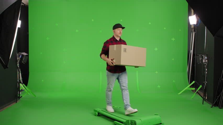 Young casual man walking on a Green Screen, Chroma Key. Man worker holding a box. Delivery concept. Forward view
