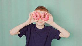 The boy fools around, shows tongue with donuts in a National doughnut day. Slow motion video.