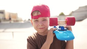 child boy with a skateboard. boy in a red cap with a skateboard on the playground portrait. skateboarder child close-up outdoors sun glare lifestyle. kid skateboarder looking at the camera
