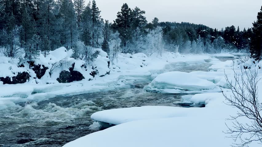Shot of Inari areas in Finland in winter. Uutua suspension bridge. Jäniskoski and the snowy path. The partially frozen river. Trekking Northern Finland near Inari typical village of Sami culture.