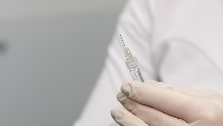 Close-up of syringe with drop (solid jelly-like soft material. hyaluronic acid filler). Preparing needle for injection on a light background. Royalty-Free Stock Footage #1100106603