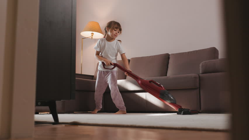 Happy Cute Little Girl Plays Uses Vacuum Cleaner. Concentrated Child cleans Carpet at home. | Shutterstock HD Video #1100107327