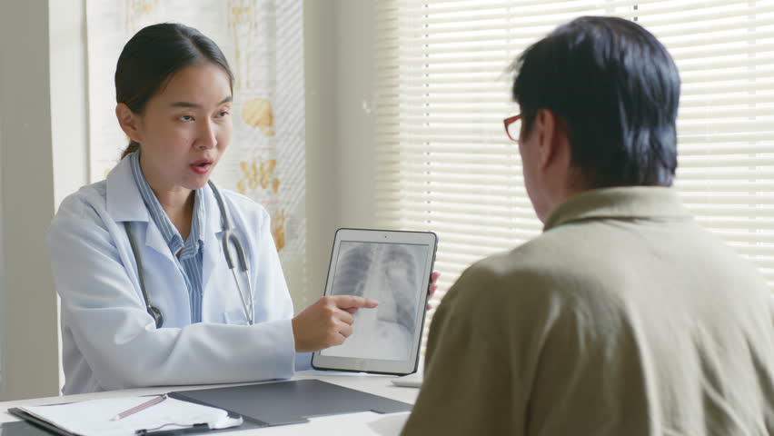 Young Asian woman doctor showing lung x-ray test results and describe to a senior patient in hospital. For cancer awareness month | Shutterstock HD Video #1100109991