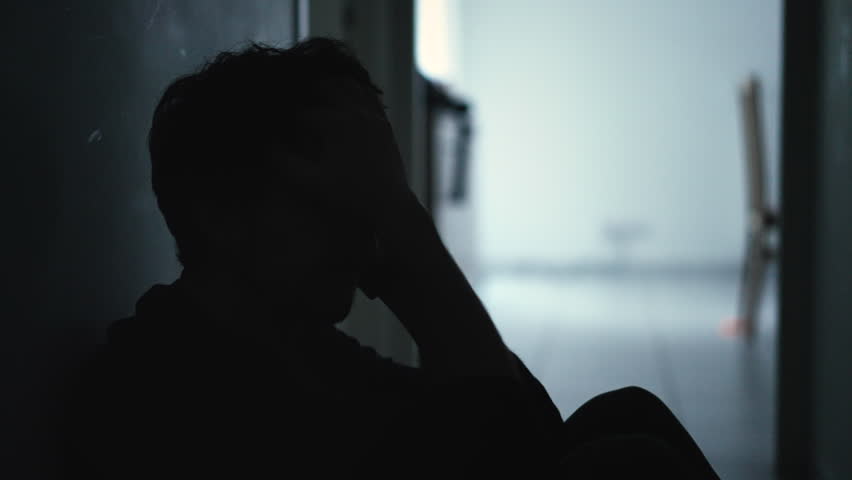 One male person covering face in shame sitting at home floor in the dark during crisis. Person suffering from depression Royalty-Free Stock Footage #1100114697