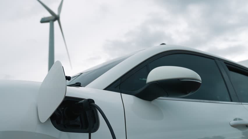 Progressive future energy infrastructure concept of electric vehicle being charged at charging station powered by green and renewable energy from a wind turbine in order to preserve the environment. | Shutterstock HD Video #1100116193
