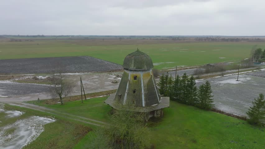 Beautiful aerial establishing view of old wooden windmill in the middle of the field, Prenclavu windmill (Otanki, Latvia), overcast winter day, wide orbiting drone shot