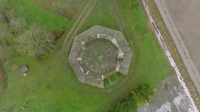 Beautiful aerial establishing view of old wooden windmill in the middle of the field, Prenclavu windmill (Otanki, Latvia), overcast winter day, descending birdseye point of interest drone shot