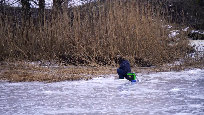 Catching fish in a hole in the ice on frozen river. Winter fishing