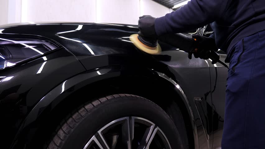 A man polishes a black car with a polishing machine in a car dealership. Car care in an auto repair shop. | Shutterstock HD Video #1100126833