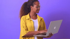 Young successful attractive African American woman entrepreneur with laptops in hands shows gesture OK to confirm one hundred everything is going according to plan stands on plain lilac background