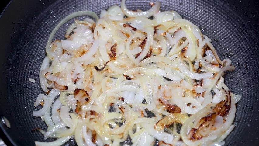 Fresh onion cut into half rings is fried in a frying pan in vegetable oil, stirring occasionally