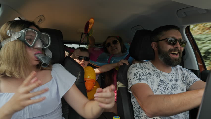 A crazy funny family with children traveling in a car. Woman in diving mask with a snorkel, everyone is having fun and dancing, enjoying their vacation, freedom | Shutterstock HD Video #1100130339