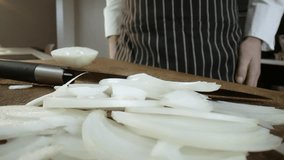 The chef works in the kitchen. Preparation of onions. Kitchen and wooden board with onions. A chef with a knife. Selective focus. Slow motion video.