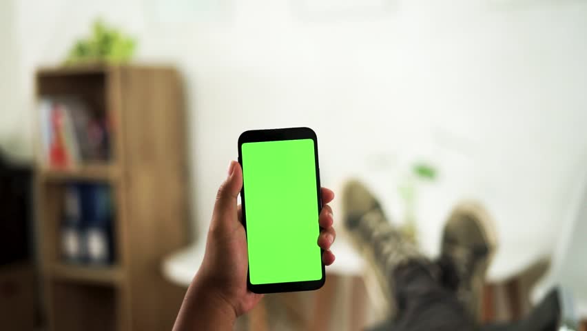 Hands holding a green screen smartphone with background of men relaxing in the living room | Shutterstock HD Video #1100133003