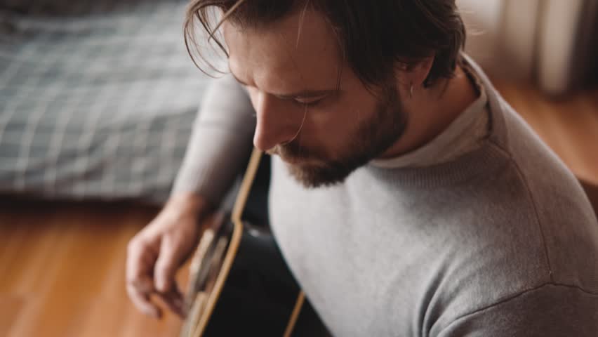 Playing the guitar. Strumming black acoustic guitar. Musician plays music. Man fingers holding mediator. Male hand playing guitar neck in dark room. Unrecognizable person rehearsing, fretboard closeup