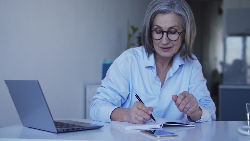 Positive retired lady writing down to do list for vacations smiling and dreaming | Shutterstock HD Video #1100134261