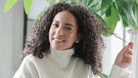Young pretty hispanic woman with white teeth dental smile relaxing at home. Happy stylish relaxed latin beautiful positive lady playing with curly hair looking at camera. Close up portrait. - Powered by Shutterstock - Get 15% off with code: PIKWIZARD15