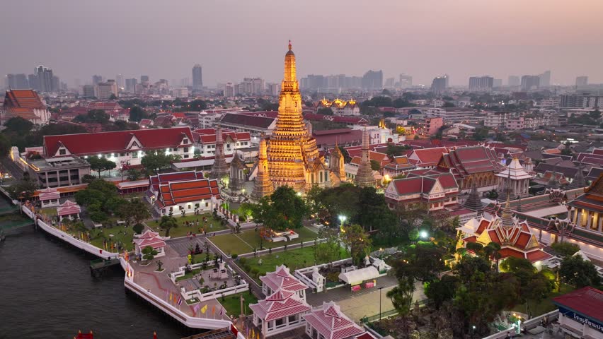 flying above Wat Arun temple in Bangkok, capital of Thailand, illuminated traditional Thai Buddhist temple of War Arun at sunset. The name of the temple is written in Thai.  Royalty-Free Stock Footage #1100136719
