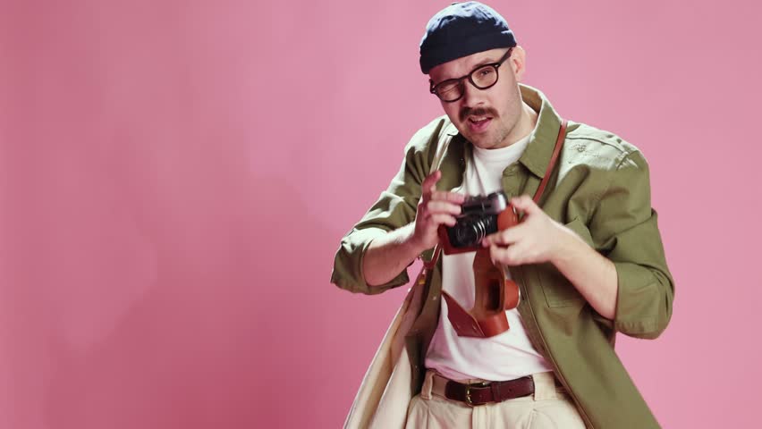 Amateur photographer, tourist. Stylish man in casual urban style clothes taking photos with vintage camera over pink studio background. Concept of emotions, lifestyle, men's fashion, mood. Ad