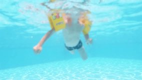 Happy boy jumped into swimming pool. Cute swimming boy in slowmotion. An underwater shot.