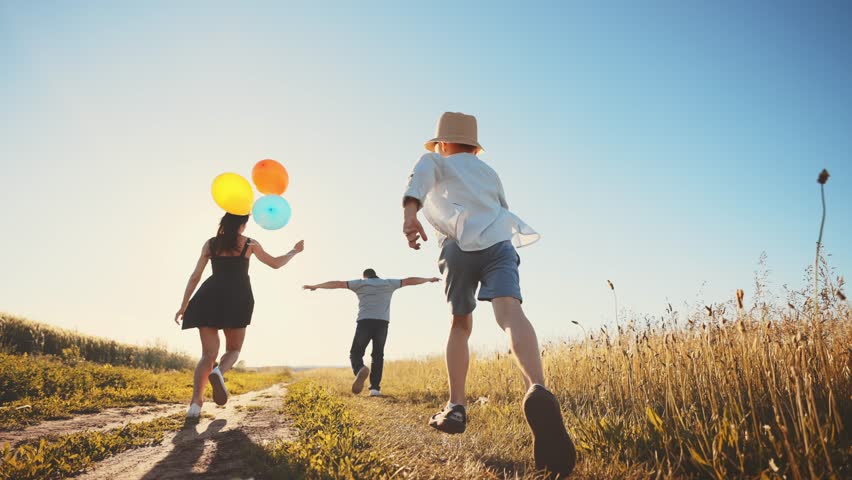 View from back of happy family: dad, mom,child running across field walk outdoors in sunny summer with balloons with arms outstretched at their sides and enjoying free and moment of life in motion. | Shutterstock HD Video #1100140627