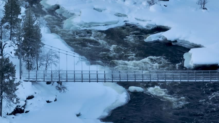 Shot of Inari areas in Finland in winter. Uutua suspension bridge. Jäniskoski and the snowy path. The partially frozen river. Trekking Northern Finland near Inari typical village of Sami culture.