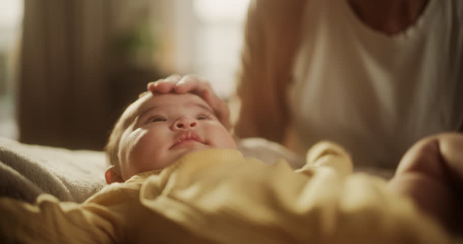 Portrait of Affectionate Asian Mother Leaning Down to Kiss her Baby who is Resting on a Bed. Woman Expressing her Motherly Love to her Infant, Thankful for the Blessing of Having her Royalty-Free Stock Footage #1100144315