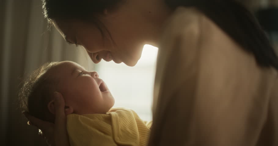 Motherly Affection Concept: Close Up Portrait of a Cute Asian Baby Laughing and Enjoying Bonding Time Together, Looking at Mother with Love. Woman New to Motherhood Having Special Moment with Infant