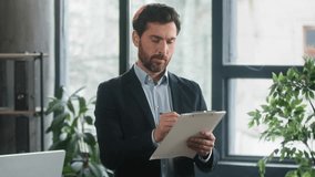 Focused adult caucasian man recruiting agent standing in office making notes writing checklist businessman conducts inspection write strategic plan showing thumb up gesture approval best choice sign - Powered by Shutterstock - Get 15% off with code: PIKWIZARD15