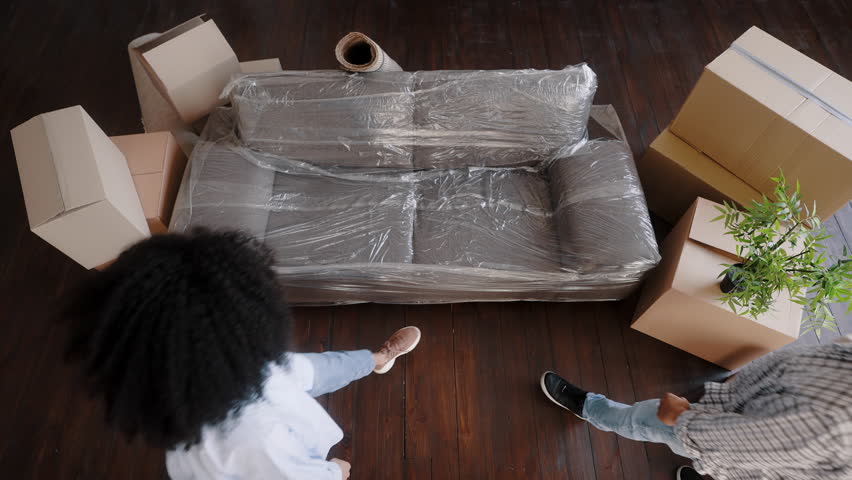 View from above of a loving couple planning housing project, the interior design of their new apartment they are moving in, sitting the sofa surrounded by cardboard boxes with packed belongings | Shutterstock HD Video #1100148281