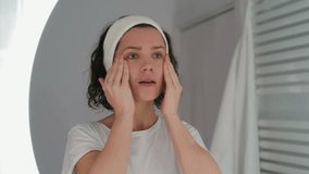 Reflection in a mirror beautiful woman washing her face and massages. Adult young girl with post acne takes care of her skin at home. Curly lady doing her morning beauty routine in white bathroom 4k - Powered by Shutterstock - Get 15% off with code: PIKWIZARD15