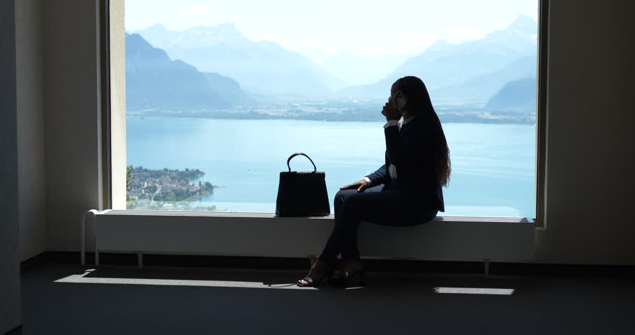 Succesful Female Sales Person on Business Travel Chatting on Mobile Phone While Looking Through Window at Lake city landscape