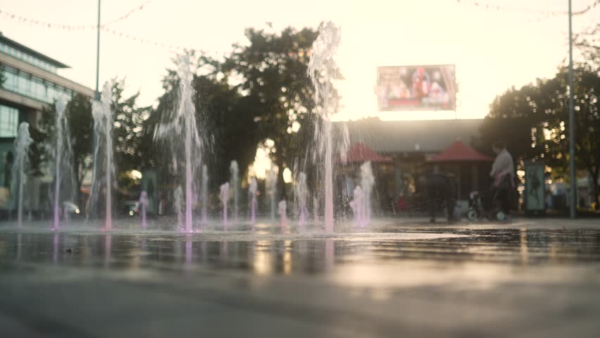 Fountains in Dundalk city center in front of a setting sun, as a family play by the water. Dundalk Ireland