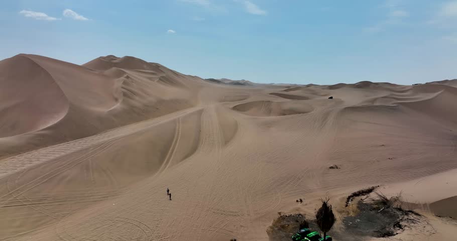 Dune buggies in Huacachina, Peru desert. Fast sand buggy driving on the sand dunes in the desert. Outdoor motorsports activities on a fun sunny day. Aerial above view drone high resolution 4k