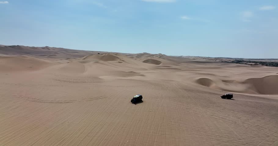 Dune buggies in Huacachina, Peru desert. Fast sand buggy driving on the sand dunes in the desert. Outdoor motorsports activities on a fun sunny day. Aerial above view drone high resolution 4k
