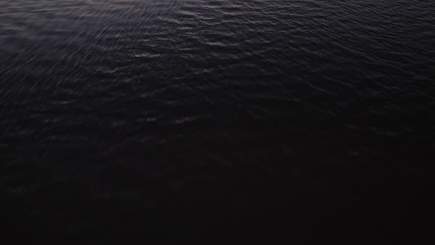 Slow drone tilt up with fast forward movement flying in from the sea over the beach in Dundalk Bay while the sun sets. Dundalk, Ireland.