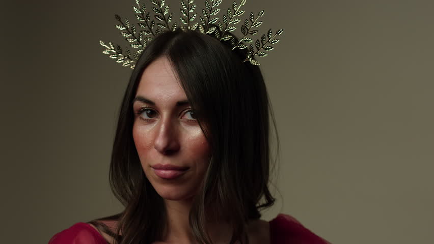 Elegant beautiful woman wearing tiara looks towards camera then up towards light - close up on face