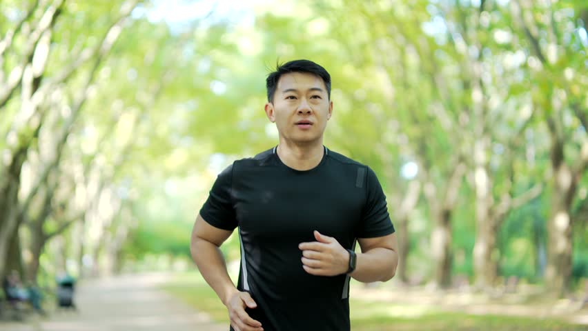 Asian runner jogging in an urban city park and looking smart watch. Man using smartwatch bracelet. Portrait of fitness man checking result. A handsome male in a sports suit enjoys running outdoors Royalty-Free Stock Footage #1100159325