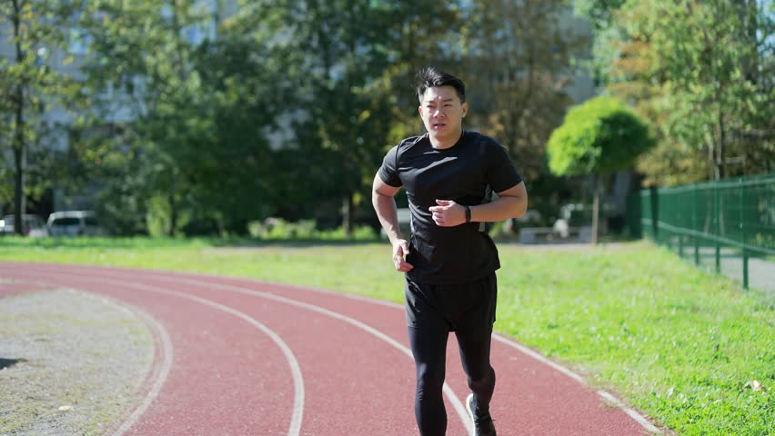 Young adult asian runner having heart attack or chest pain after running workout on treadmill in urban city stadium. A tired athlete suffers from tension in the heart. Health care and sports concept Royalty-Free Stock Footage #1100159383