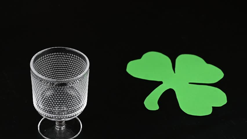 glass being filled with green alcoholic drink with black background and shamrock for st patricks day celebration. Irish holiday is popular drinking event when people party and consume large quantities