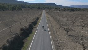 Young woman is riding s a road bike on the rural road with top front view drone video.Cycling in the mountains.Sport mood motivational aerial video. 4k drone footage Murcia, Spain