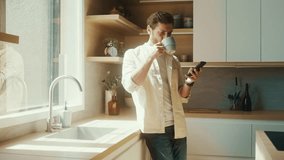 Caucasian man standing near window in modern interior apartment sunny kitchen having morning coffee scrolling news feed on phone. Business man using smartphone
in his home office.  - Powered by Shutterstock - Get 15% off with code: PIKWIZARD15