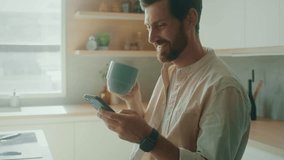 Happy Caucasian man sitting on chair in modern interior apartment sunny kitchen enjoy morning coffee scrolling news feed on phone. Business man using smartphone
in his home office.  - Powered by Shutterstock - Get 15% off with code: PIKWIZARD15