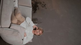 Vertical video of an old cheerful happy woman having fun talking on the phone while staying at home. An elderly woman is talking to her friends on the phone from home. High quality 4k footage