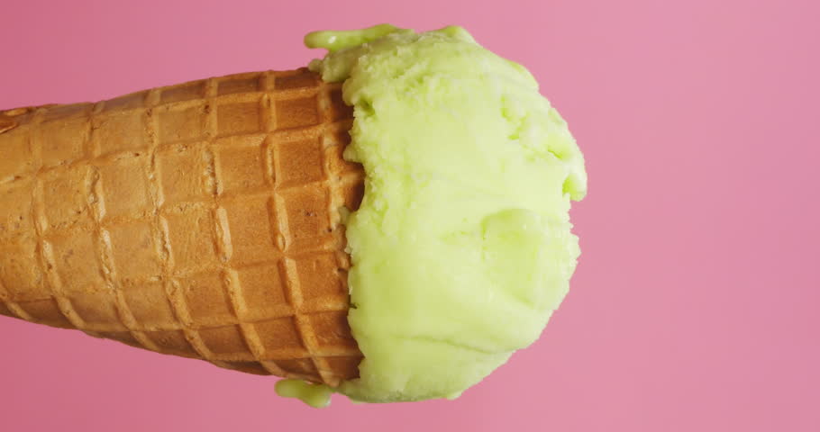 Vertical Time Lapse Video, Fresh green lemon flavored ice cream in cone on pink background slowly melting, delicious ice cream concept.