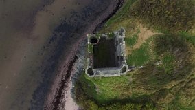 Topdown ascending aerial video of a ruined stone tower on the edge of a cliff and gradually revealing the sea