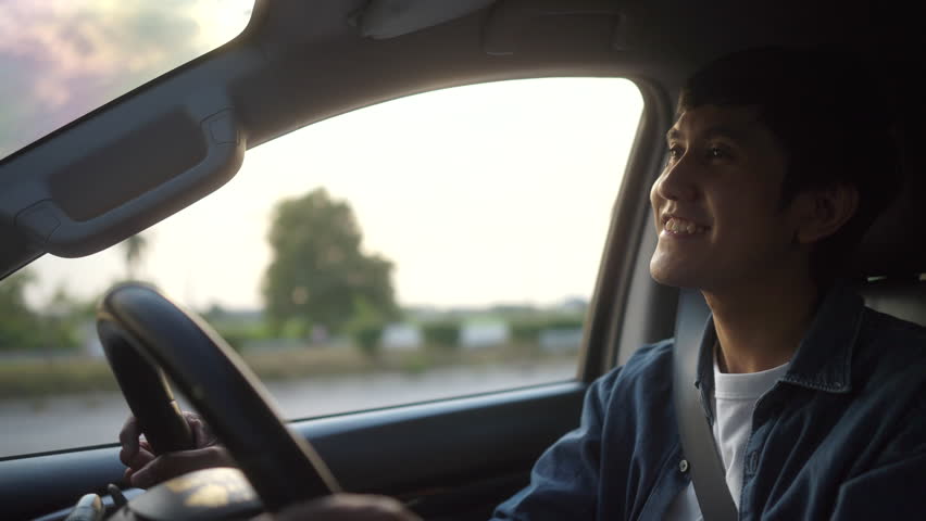 Happy young asian man looking roadway while driving car in the morning. Man sitting in car was feeling proud and very happy.